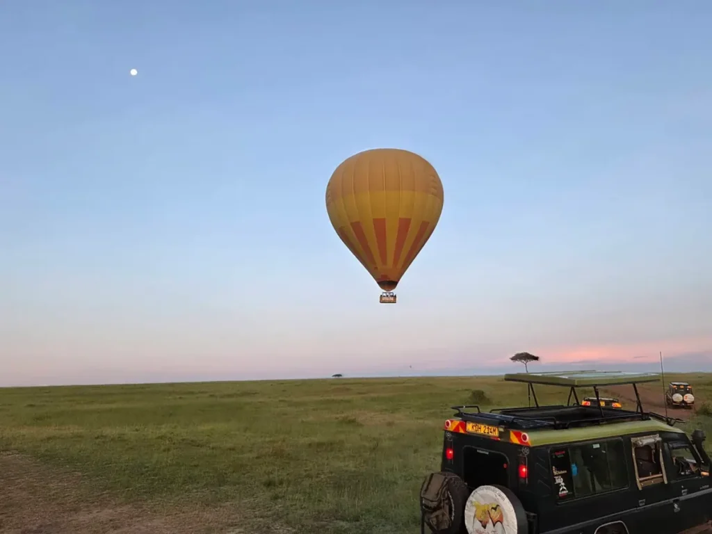 A hot-air balloon above the plains with a safari vehicle in the foreground