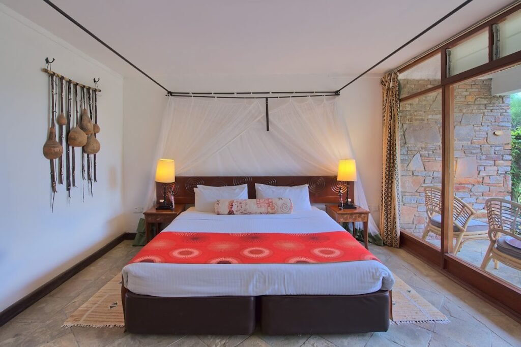 Bedroom with a mosquito net, carved wooden headboard and terrace doors at Keekorok Lodge