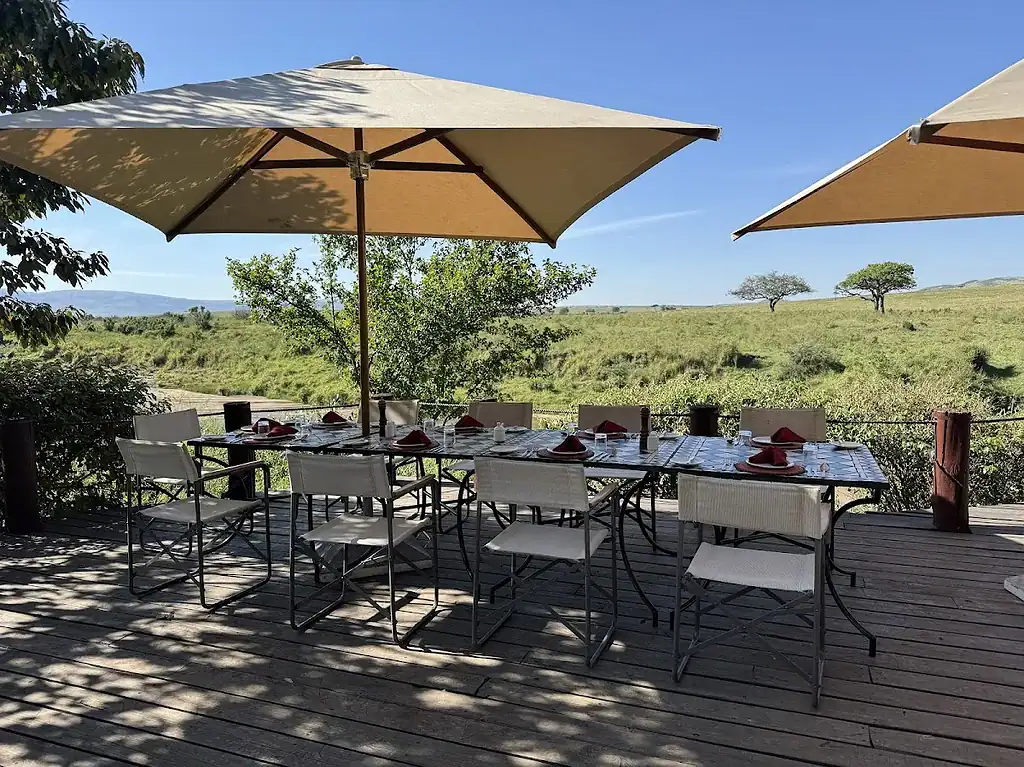 Bush dining in the Maasai Mara: breakfast, dinner and sundowners 2 Dining tables under umbrellas on a camp deck overlooking grassland