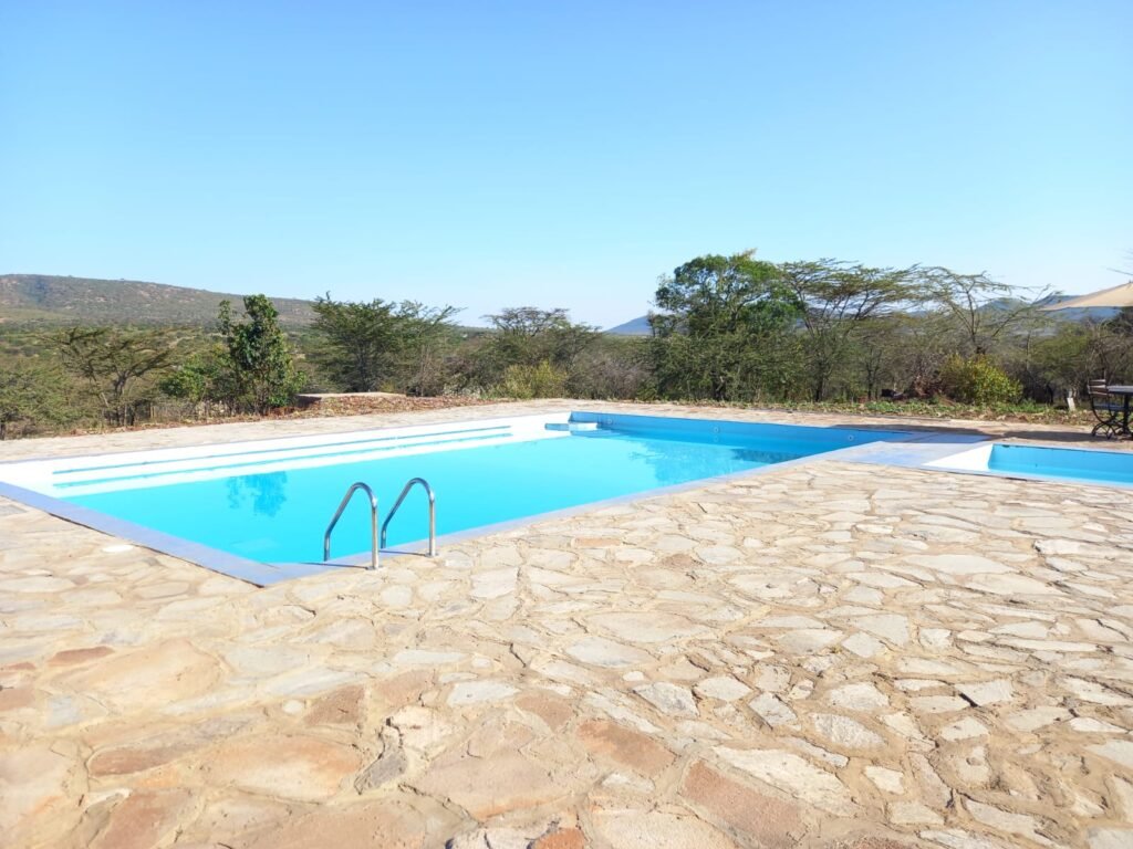 Elangata Olerai Tented Camp outdoor swimming pool with a stone terrace, trees and distant hills