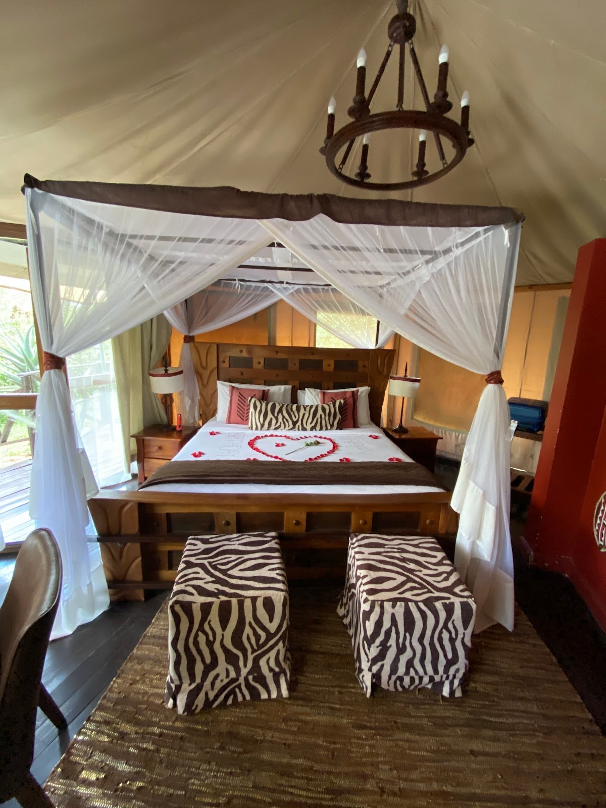 Emayian Luxury Camp tent bedroom with canopy, wooden bed and zebra-pattern stools
