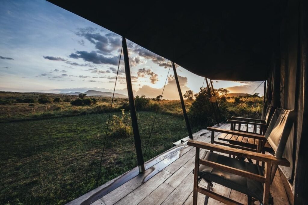 Maasai Mara lodges and camps 20 Enkewa Camp tent veranda with wooden chairs overlooking grassland at sunset