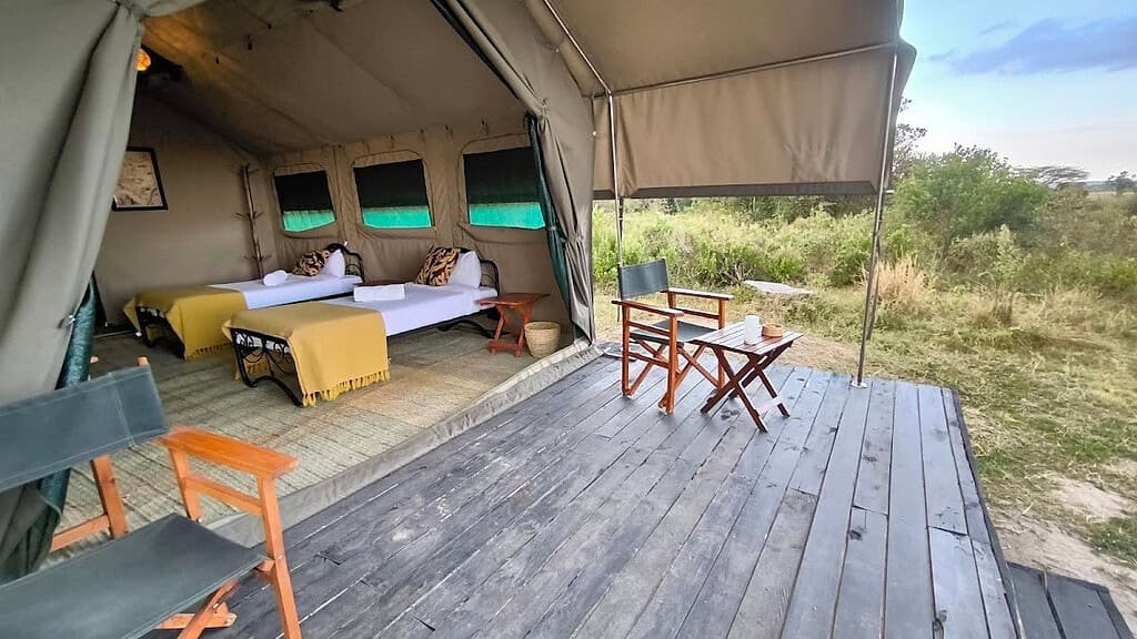 Safari tent bedroom opening onto a raised deck with chairs and a table