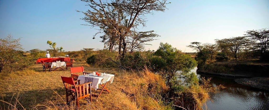 Tables set beside a river for bush dining at Olare Mara Kempinski