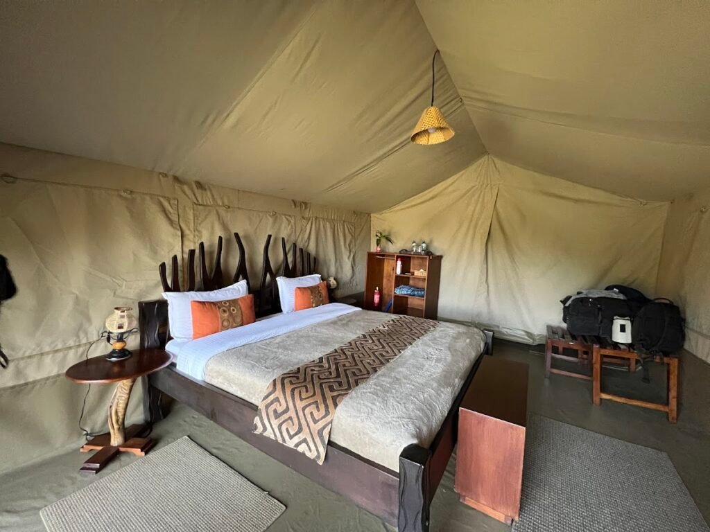 Maasai Mara lodges and camps 67 Mara River Camp canvas tent bedroom with a timber bed and orange cushions