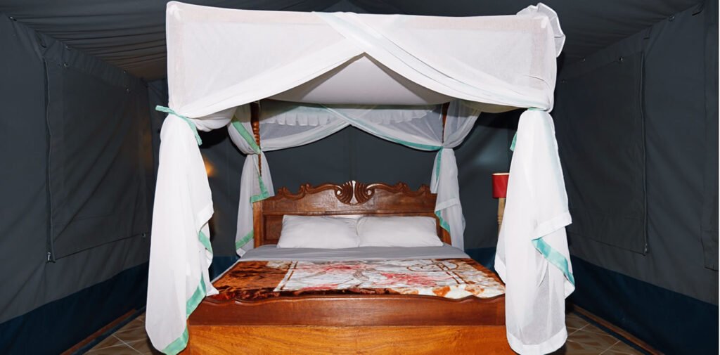 Miti Mingi Eco Camp tent interior with a wooden double bed and white mosquito net