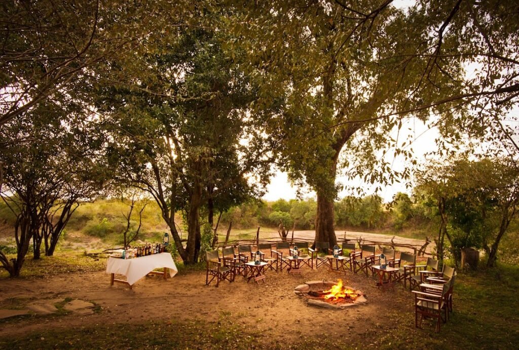 Evening fire setting in a wooded Maasai Mara camp landscape
