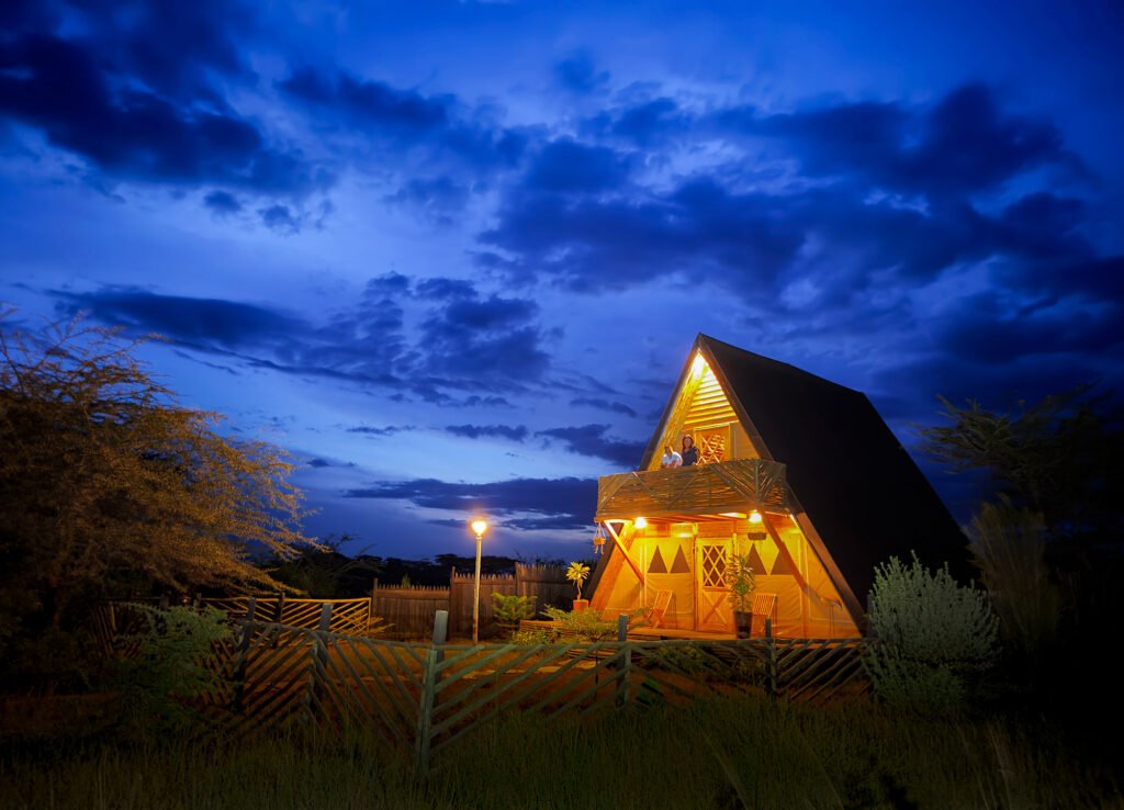 Maasai Mara lodges and camps 97 Osero Sopia River Camp illuminated A-frame accommodation with a timber balcony at dusk