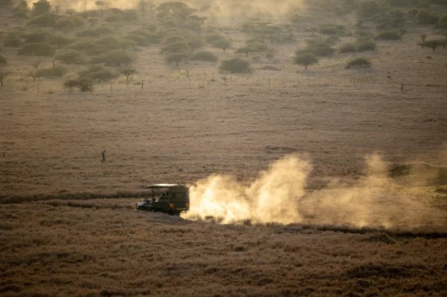 Maasai Mara packing list guide: safari vehicle raising dust on a dry grassland track