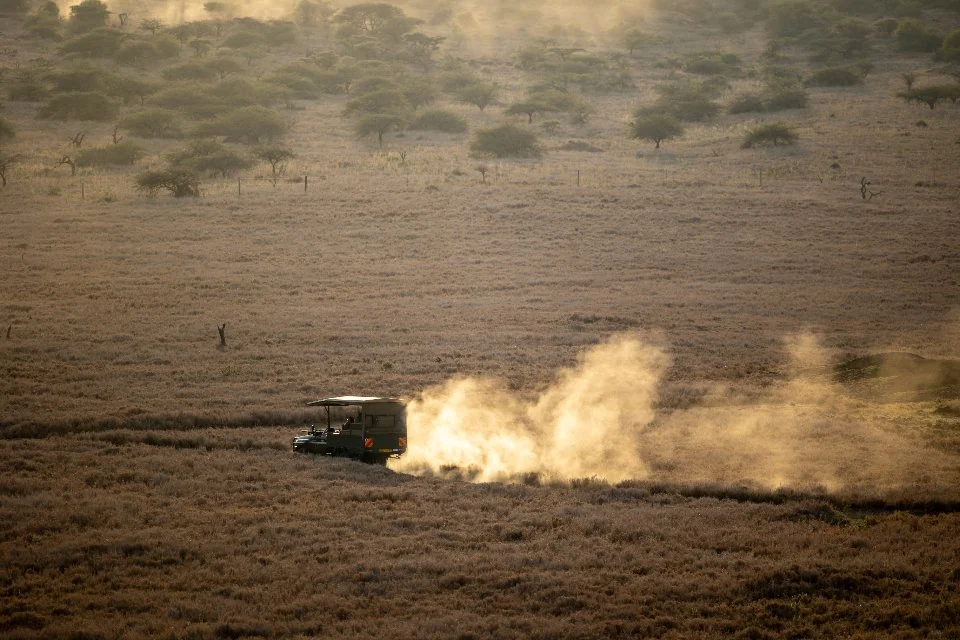 Maasai Mara packing list guide: safari vehicle raising dust on a dry grassland track