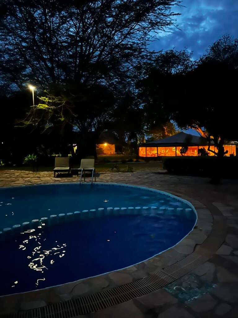 Maasai Mara lodges and camps 74 Mara Sweet Acacia Lodge swimming pool and illuminated communal building at dusk