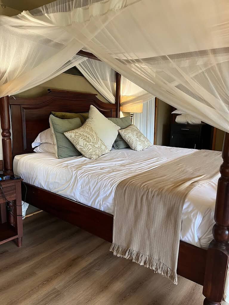 Canvas guest tent with a wooden bed and mosquito net at Elewana Sand River Maasai Mara